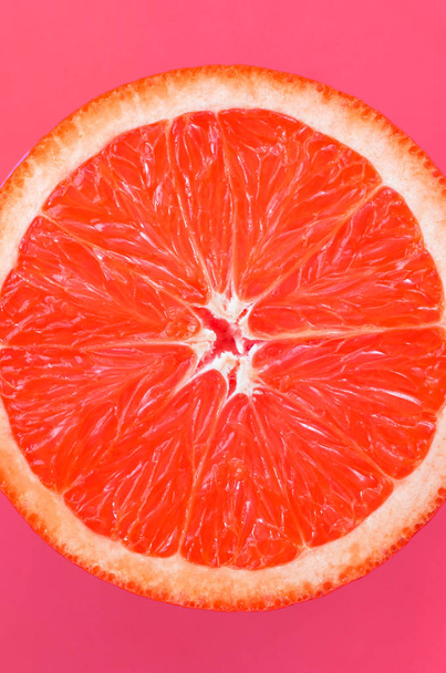 Top view of a one grapefruit slice on bright background in light pink color. A saturated citrus texture image - Fotoğraf, Görsel