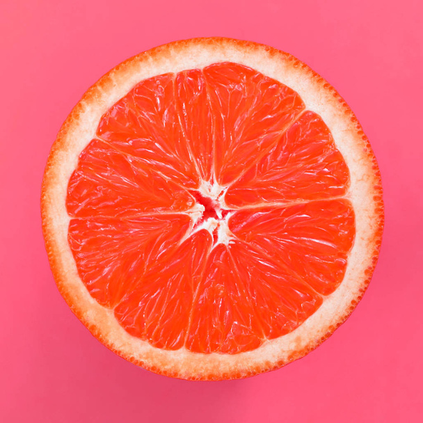 Top view of a one grapefruit slice on bright background in light pink color. A saturated citrus texture image - Zdjęcie, obraz