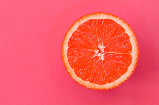Top view of a one grapefruit slice on bright background in light pink color. A saturated citrus texture image - Photo, Image