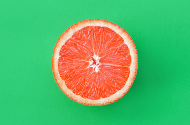 Top view of an one grapefruit slice on bright background in green color. A saturated citrus texture image - Fotografie, Obrázek