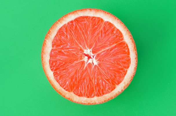 Top view of an one grapefruit slice on bright background in green color. A saturated citrus texture image - Photo, Image