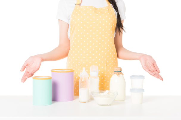обрезанный снимок женщины в фартуке с широкими руками, стоящими за столом с детским питанием и молоком на белом фоне
  - Фото, изображение