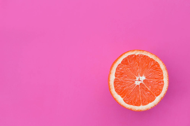 Bovenaanzicht van een segment van een grapefruit op lichte achtergrond in paarse kleur. Een verzadigde citrus textuur afbeelding - Foto, afbeelding