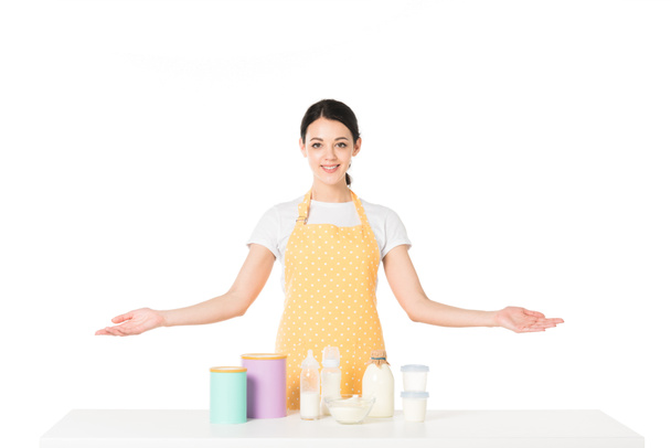 smiling woman with wide arms standing at table with children food and milk isolated on white background  - Photo, Image