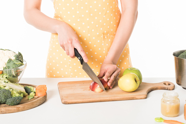 περικομμένη εικόνα της γυναίκας στην ποδιά κοπής apple από μαχαίρι που απομονώνονται σε λευκό φόντο  - Φωτογραφία, εικόνα