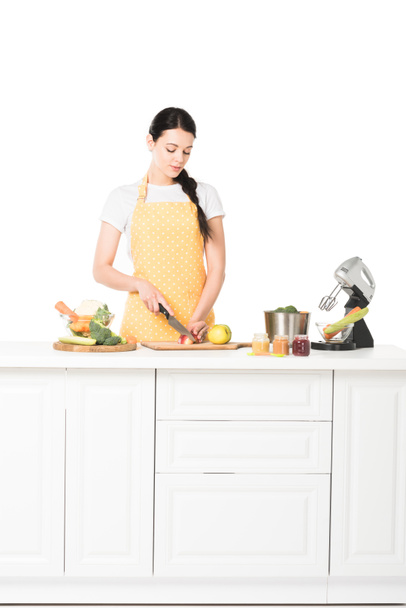 femme dans tablier coupe pomme à table avec mélangeur, casserole, pots, fruits et légumes
  - Photo, image