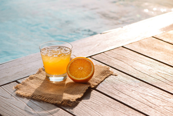 Close up of cocktail with orange juice and ice near pool - Zdjęcie, obraz