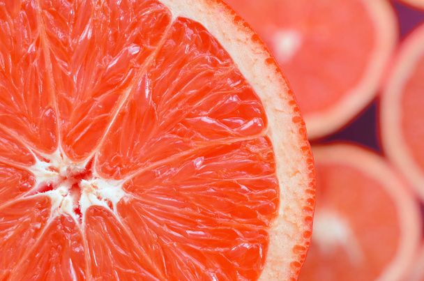 Pohled shora fragment plátku červeného grapefruitu na pozadí mnoha rozmazané grapefruitové řezy. Nasycený citrusových textury obrazu - Fotografie, Obrázek
