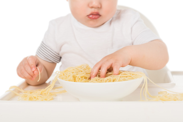 手でスパゲッティを食べ、ハイチェアに座っている男の子の赤ちゃんのショットをトリミング  - 写真・画像
