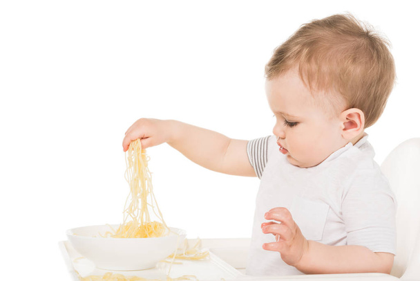 side view of adorable little boy eating spaghetti by hand isolated on white background  - Photo, image