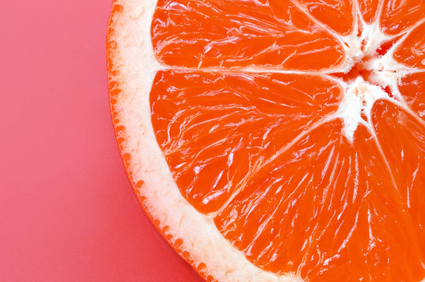 Top view of a one grapefruit slice on bright background in light pink color. A saturated citrus texture image - Fotografie, Obrázek