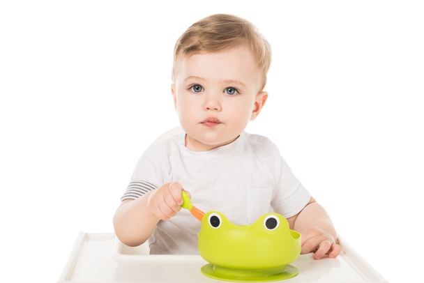 очаровательный маленький мальчик ест из тарелки в виде лягушки и сидит в кресле
  - Фото, изображение