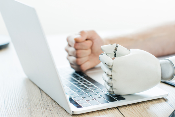 Nahaufnahme von Menschen- und Roboterfäusten auf Laptop am Holztisch - Foto, Bild