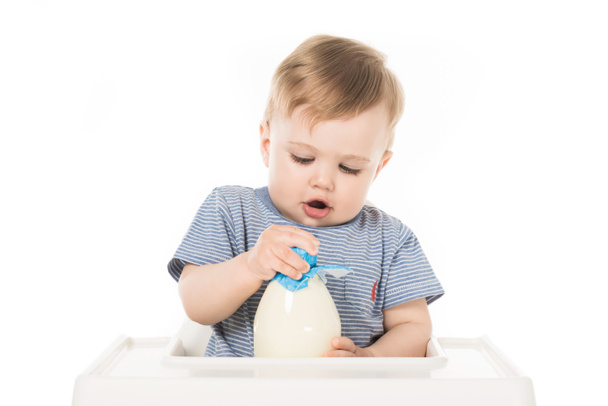 little boy trying to open bottle of milk and sitting in highchair isolated on white background  - Zdjęcie, obraz