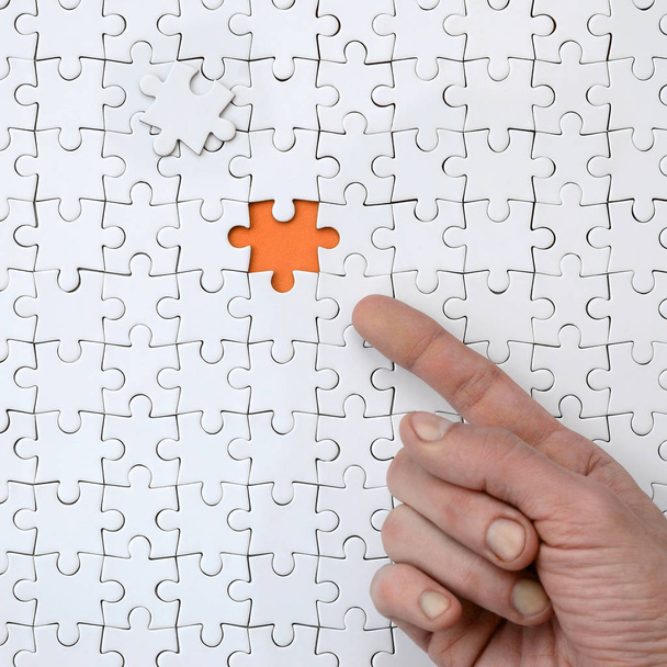 La trama di un puzzle bianco nello stato assemblato con un elemento mancante, formando uno spazio arancione, indicato dal dito della mano maschile
 - Foto, immagini