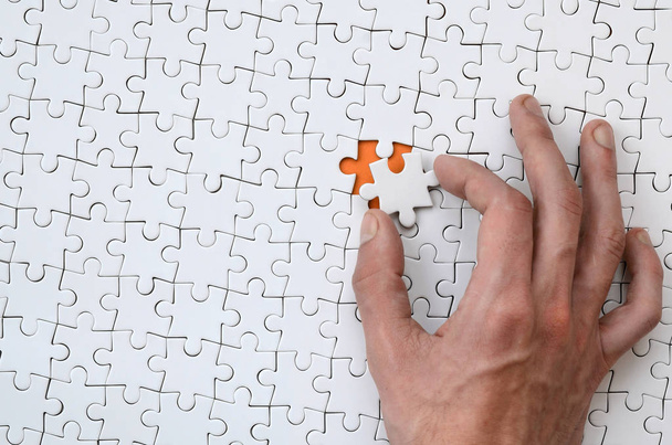 La texture d'un puzzle blanc à l'état assemblé avec un élément manquant que la main masculine met en
 - Photo, image