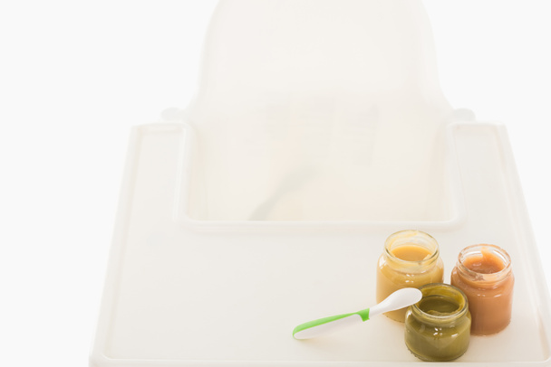 vue grand angle de trois bocaux avec purée d'enfant et cuillère sur chaise haute isolé sur fond blanc
  - Photo, image