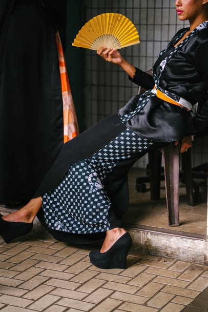 Fashion portrait of an attractive, intense Muslim model. She is wearing a silky kimono , she sits in a chair on a street in Asia. - Foto, Imagem