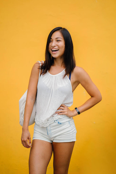 Portrait of an athletic, cute Chinese Asian girl dressed comfortably and smiling at the camera against a yellow background in a studio. - Фото, зображення