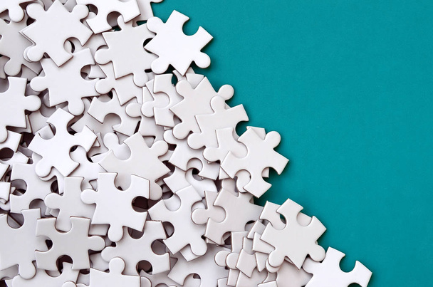 A pile of uncombed elements of a white jigsaw puzzle lies on the background of a blue surface. Texture photo with copy space for text - Photo, Image