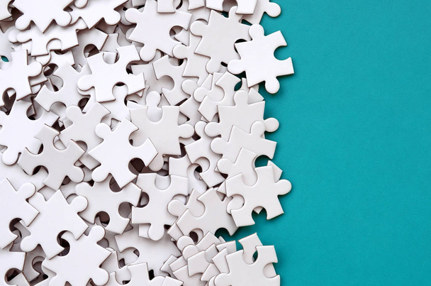 A pile of uncombed elements of a white jigsaw puzzle lies on the background of a blue surface. Texture photo with copy space for text - Photo, Image