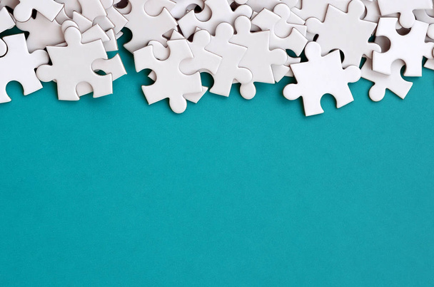 A pile of uncombed elements of a white jigsaw puzzle lies on the background of a blue surface. Texture photo with copy space for text - Foto, imagen