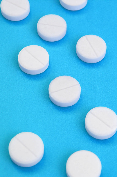 Kilka białych tabletek leżą na powierzchni jasne niebieskie tło. Obraz tła na tematy medyczne i farmaceutyczne - Zdjęcie, obraz