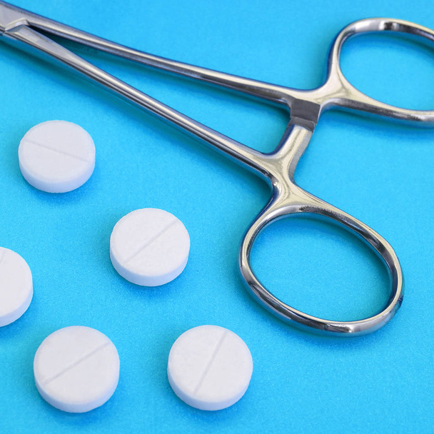 Несколько белых таблеток и медицинский зажим лежат на ярко-синем фоне. Фон изображения на медицинские и фармацевтические темы
 - Фото, изображение