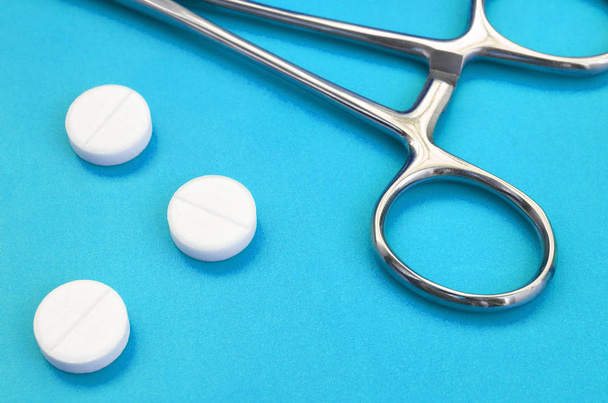 Несколько белых таблеток и медицинский зажим лежат на ярко-синем фоне. Фон изображения на медицинские и фармацевтические темы
 - Фото, изображение