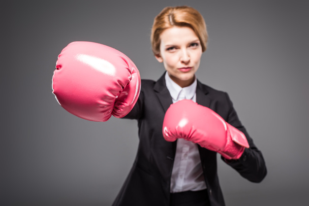 selective focus of businesswoman in suit and pink boxing gloves, isolated on grey - Fotografie, Obrázek