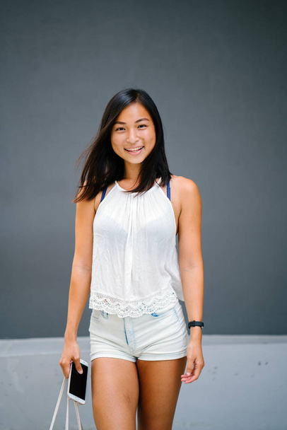 Portrait of a cute, athletic, tanned Asian Chinese girl walking on the street against a grey background. - Foto, afbeelding