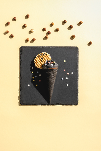 top view of black ice cream and scattered hazelnuts on yellow - Foto, immagini