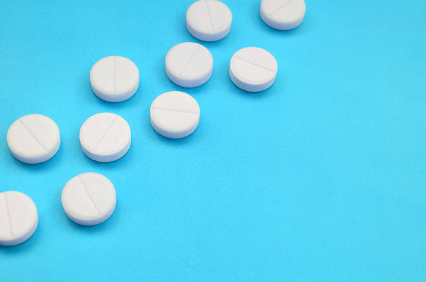 A few white tablets lie on a bright blue background surface. Background image on medical and pharmaceutical topics - Foto, Imagem