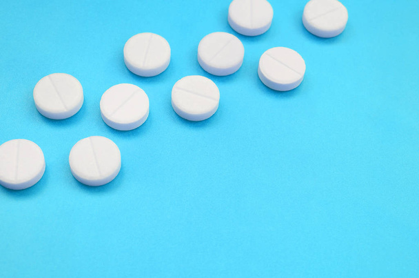A few white tablets lie on a bright blue background surface. Background image on medical and pharmaceutical topics - Photo, Image