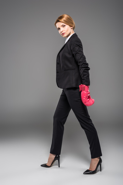 serious businesswoman in suit and pink boxing gloves, isolated on grey - Zdjęcie, obraz