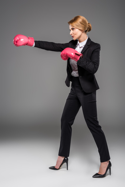 executive businesswoman in suit and pink boxing gloves, isolated on grey - Фото, зображення