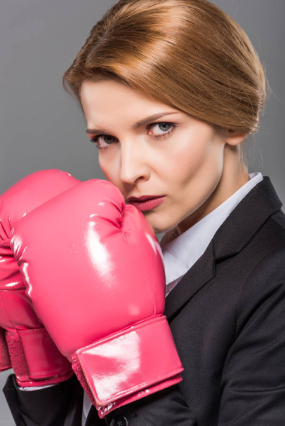 serious businesswoman in suit and pink boxing gloves, isolated on grey - Foto, Imagem