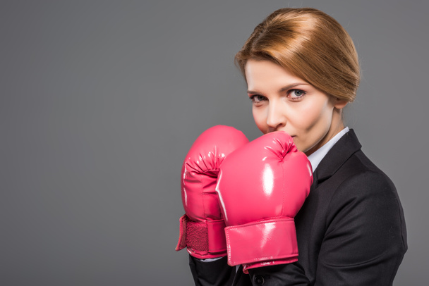 attractive businesswoman in suit and pink boxing gloves, isolated on grey - Фото, зображення
