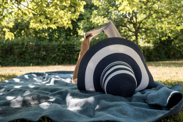 Femme allongée sur un tapis à l'ombre d'un arbre lisant un livre
 - Photo, image