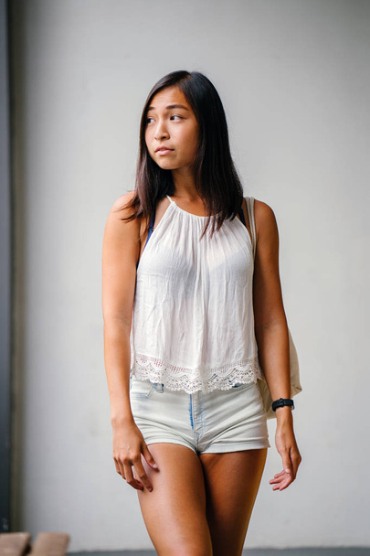 Portrait of a cute, athletic, tanned Asian Chinese girl walking on the street against a grey background. - Foto, Imagem