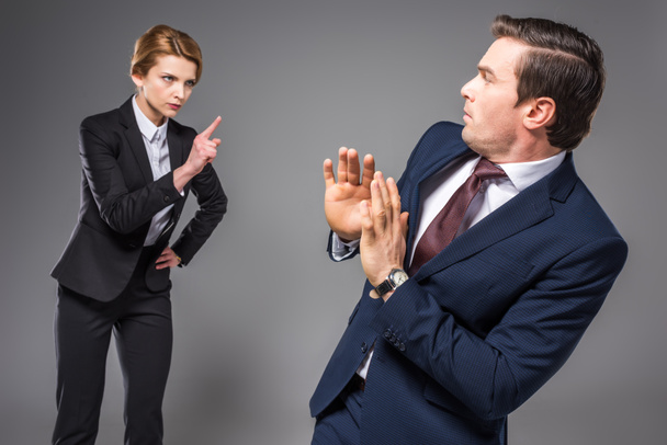 aggressive businesswoman quarreling and pointing at scared businessman, isolated on grey - Photo, Image