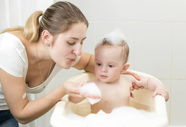 Portrait of young mother playing with her toddler boy washing in bathroom with foam - Foto, Imagem