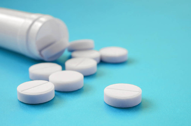 Several white tablets fall out of the plastic jar on the blue surface. Background image on medical and pharmaceutical topics - Photo, Image
