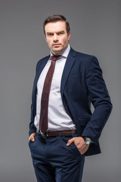 handsome businessman in formal wear with hands in pockets, isolated on grey - Foto, Imagem