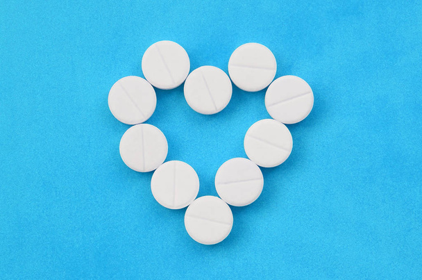 Varios comprimidos blancos se encuentran sobre un fondo azul brillante en forma de corazón. Imagen de fondo sobre temas de medicina y farmacéutica
 - Foto, imagen