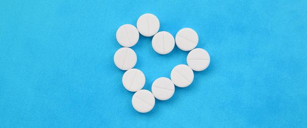 Birkaç beyaz tabletler parlak mavi bir arka plan bir kalp şeklinde yalan. Tıp ve eczacılık konularda arka plan görüntüsü - Fotoğraf, Görsel