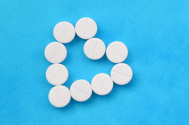 Několik bílých tablet leží na světle modrém pozadí ve tvaru srdce. Obrázek na pozadí medicíny a farmaceutické témata - Fotografie, Obrázek