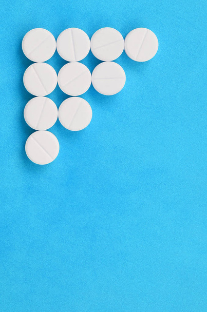 Vários comprimidos brancos encontram-se sobre um fundo azul brilhante na forma de uma seta triangular. Imagem de fundo sobre medicina e tópicos farmacêuticos
 - Foto, Imagem
