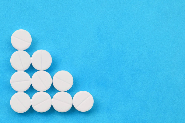 Auf einem hellblauen Hintergrund in Form eines dreieckigen Pfeils liegen mehrere weiße Tabletten. Hintergrundbild zu medizinischen und pharmazeutischen Themen - Foto, Bild
