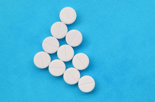 Varios comprimidos blancos se encuentran sobre un fondo azul brillante en forma de flecha triangular. Imagen de fondo sobre temas de medicina y farmacéutica
 - Foto, Imagen